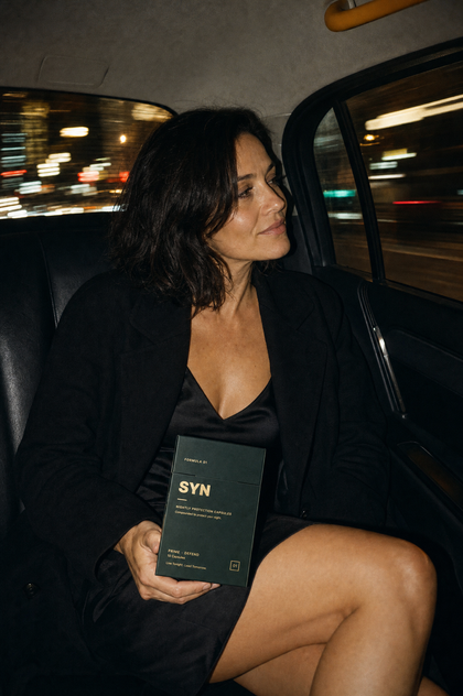 A woman in the back of a taxi at night, holding a box of SYN